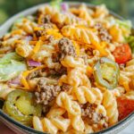 A bowl of Creamy Big Mac Pasta Salad with beef, pickles, cheddar cheese, lettuce, and tomatoes.