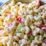 A close-up shot of Creamy Classic Macaroni Salad, featuring elbow macaroni mixed with a creamy dressing, diced tomatoes, red onion, and celery.