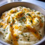 A close-up of a bowl of creamy potato soup, topped with melted cheddar cheese and fresh parsley.