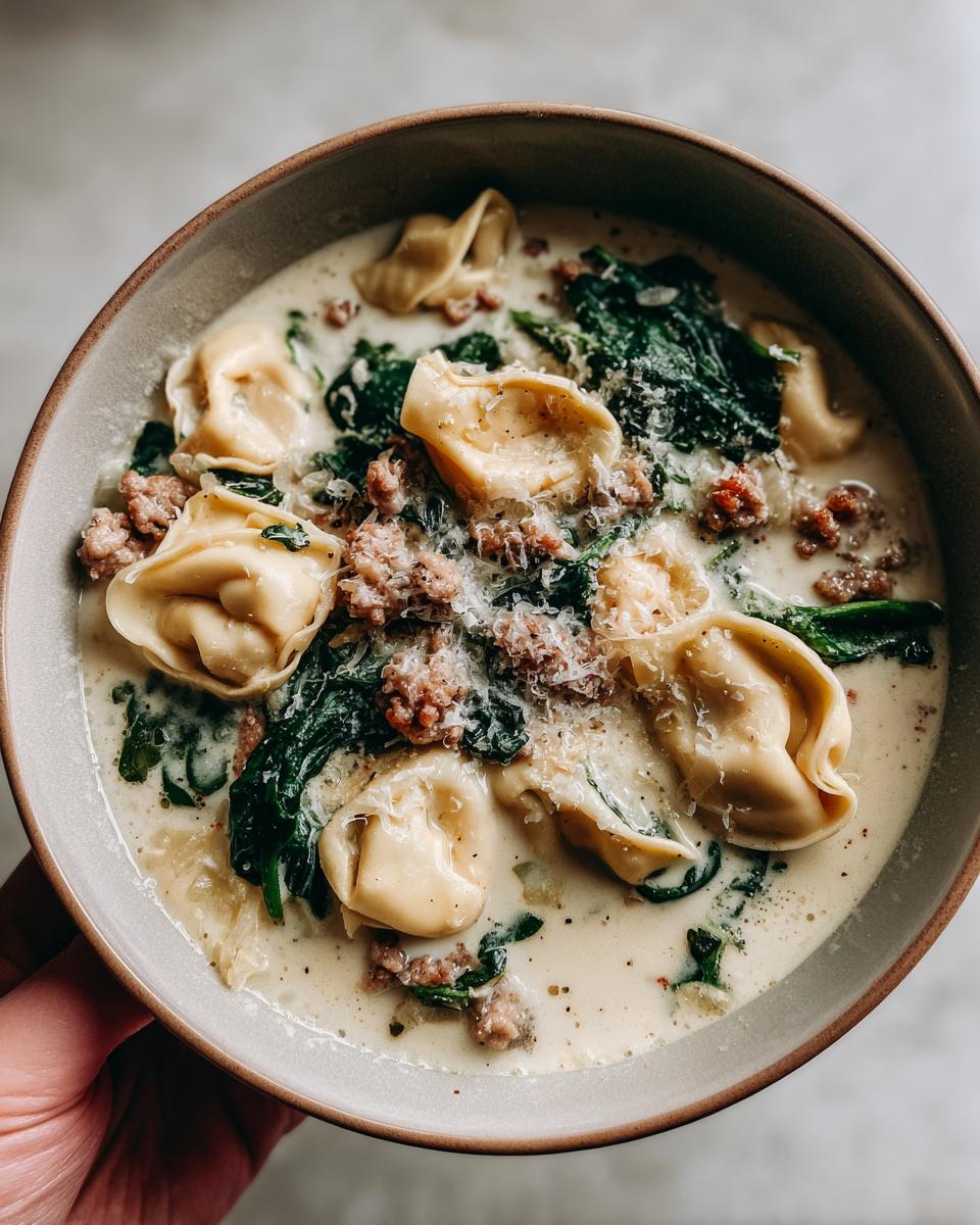 A close-up shot of a bowl filled with creamy sausage tortellini soup, featuring tortellini pasta, spinach, and crumbled sausage.