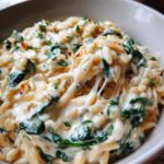 A close-up of creamy spinach orzo with melted cheese stretching, garnished with parsley.