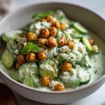 A close-up of a refreshing cucumber salad with crispy chickpeas, feta cheese, and fresh dill and mint.