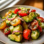A vibrant and fresh cucumber tomato avocado salad with red onion and parsley, tossed in a light dressing.