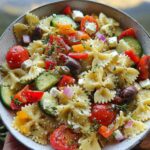 A bowl of Easy Greek Pasta Salad with Feta and Lemon Dressing, featuring farfalle pasta, cherry tomatoes, cucumber, olives, feta, and red onion.