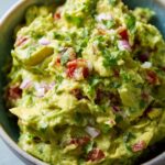 Close-up of a bowl filled with chunky, fresh easy guacamole, topped with cilantro and red onion.