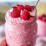 Close-up of a jar of Easy Raspberry Chia Pudding with Maple Syrup, topped with fresh raspberries and slivered almonds.