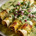 Close-up of three enchiladas suizas smothered in a creamy green sauce and topped with fresh cilantro and red onion.