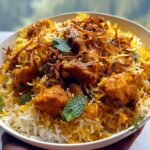 A close-up of a bowl filled with Fragrant Butter Chicken Biryani, showcasing tender chicken pieces, fluffy rice, and fresh mint leaves.