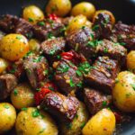 Close-up of juicy garlic butter steak and potatoes cooked together in a skillet, garnished with fresh parsley.