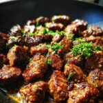 Close-up of juicy garlic butter steak bites in a pan, garnished with fresh parsley and chili flakes.