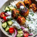 A close-up of delicious Greek meatball bowls, featuring seasoned meatballs, fluffy rice, fresh cucumber, cherry tomatoes, red onion, and creamy tzatziki sauce.