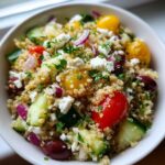 A vibrant bowl of Greek quinoa salad featuring quinoa, cherry tomatoes, cucumber, olives, red onion, and feta cheese.