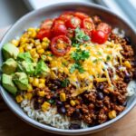 A delicious bowl of ground turkey taco bowls with rice, black beans, corn, avocado, tomatoes, and cheese.