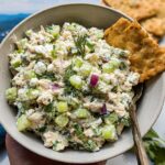 A bowl of Healthy Tzatziki Chicken Salad with Greek Yogurt, filled with chicken, cucumber, celery, red onion, and herbs, served with crackers.