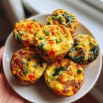 A plate of six savory high protein egg muffins filled with spinach, red peppers, and cheese, garnished with green onions.