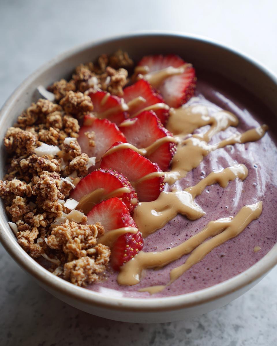 A vibrant high protein smoothie bowl topped with fresh strawberries, crunchy granola, and a drizzle of peanut butter.