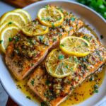 Close-up of three perfectly cooked honey garlic baked salmon fillets topped with lemon slices and fresh parsley.