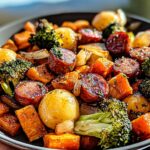 A close-up of a Honey Garlic Chicken Sausage Sheet Pan meal featuring roasted sausage, broccoli, sweet potatoes, and onions.