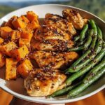 A plate of Honey Garlic Chicken and Sweet Potato with green beans, drizzled with sauce and sprinkled with sesame seeds.