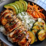 A close-up of delicious hot honey chicken and rice bowls, featuring sliced chicken, rice, avocado, zucchini, and carrots.