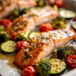 Close-up of baked lemon garlic salmon fillets with roasted cherry tomatoes, broccoli, and zucchini.