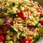 Close-up of a vibrant lemon orzo salad with cherry tomatoes, cucumber, red onion, and feta cheese.