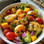 A close-up of a vibrant mango avocado shrimp salad in a white bowl, featuring plump shrimp, diced mango, avocado, cherry tomatoes, and red onion.