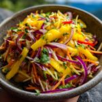 A close-up of a colorful Mango slaw in a rustic bowl, featuring shredded mango, carrots, red onion, and cilantro.
