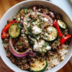 A close-up of a Mediterranean beef skillet bowl with rice, ground beef, zucchini, red onion, bell pepper, and feta cheese.