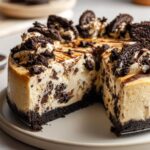 A slice of no bake Oreo cheesecake with a chocolate cookie crust and Oreo chunks throughout.