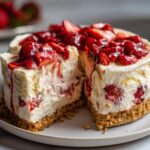 A slice of no bake strawberry cheesecake with a graham cracker crust and fresh strawberry topping.