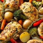 Close-up of a delicious one pan lemon herb chicken and veggies dish with roasted chicken breasts, potatoes, broccoli, carrots, and red peppers.