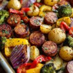 Close-up of a sheet pan sausage and veggies dinner with roasted potatoes, broccoli, bell peppers, and red onion.