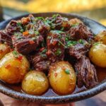 A close-up of Slow Cooker Garlic Butter Beef and Potatoes in a bowl, garnished with fresh herbs.