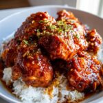 A bowl of fluffy white rice topped with glistening slow cooker honey garlic chicken, garnished with herbs.