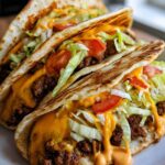 Close-up of two fully loaded smash burger tacos, featuring seasoned ground beef, melted cheese, shredded lettuce, and diced tomatoes.