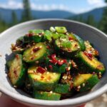 A close-up of a bowl of Spicy Asian Cucumber Salad, garnished with sesame seeds and scallions.