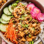 Close-up of a delicious Spicy Bang Bang Ground Turkey Rice Bowl with cucumber, carrots, edamame, and pickled radish.