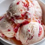 Close-up of creamy strawberry ice cream scoops in a white bowl, swirled with vibrant strawberry pieces.