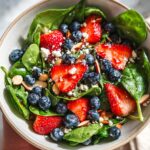 A vibrant strawberry spinach salad topped with fresh blueberries, crumbled feta cheese, and sliced almonds.