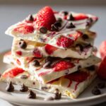 A stack of delicious strawberry yogurt bark pieces topped with fresh strawberries and chocolate chips.
