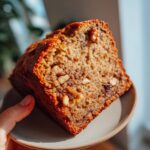 A close-up of a slice of Super Moist Banana Bread, showing its moist texture and chunks of walnuts.