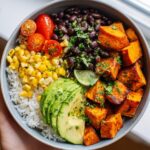 A vibrant Sweet Potato Black Bean Bowl featuring rice, black beans, corn, avocado, cherry tomatoes, and lime.