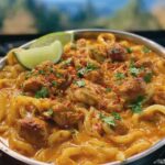 A close-up of Thai Coconut Red Curry Chicken Udon, featuring tender chicken pieces and thick udon noodles in a rich, creamy red curry sauce, garnished with lime and cilantro.