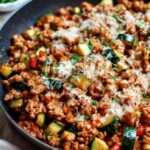 Close-up of a turkey zucchini skillet meal topped with melted cheese and fresh parsley.