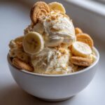 A bowl of creamy Banana Pudding Ice Cream No Churn topped with banana slices, vanilla wafers, and cookie crumbs.