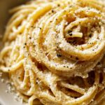 Close-up of a swirl of spaghetti coated in creamy sauce and black pepper for a Cacio E Pepe Recipe.