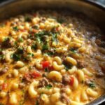 A close-up view of a steaming pot of Cheeseburger Macaroni Soup, filled with elbow macaroni, ground beef, and tomatoes, garnished with parsley.