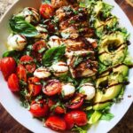 A vibrant Chicken Avocado Caprese Salad featuring sliced grilled chicken, avocado, cherry tomatoes, and mozzarella balls, drizzled with balsamic glaze.