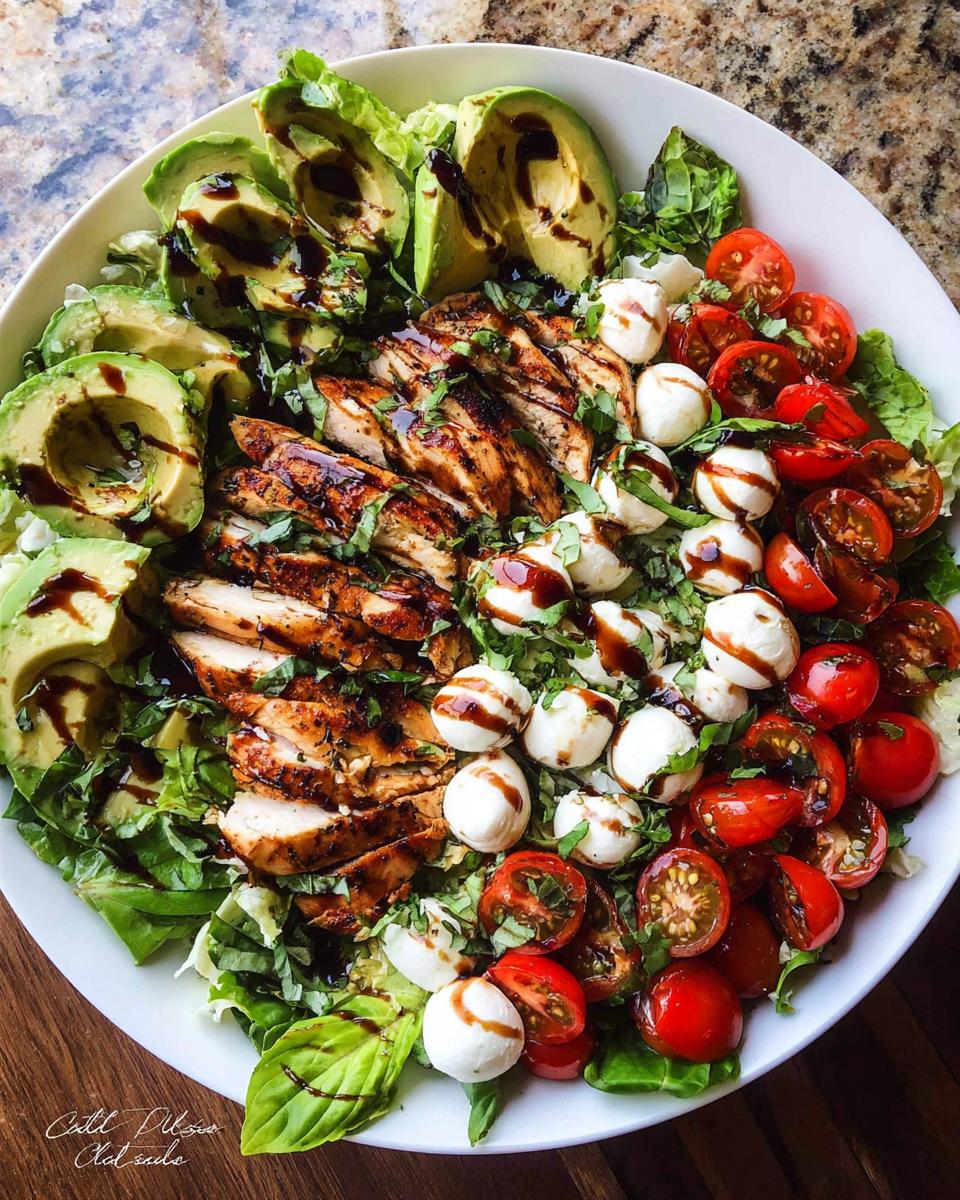 A vibrant Chicken Avocado Caprese Salad featuring grilled chicken, avocado slices, cherry tomatoes, and mozzarella balls, drizzled with balsamic glaze.
